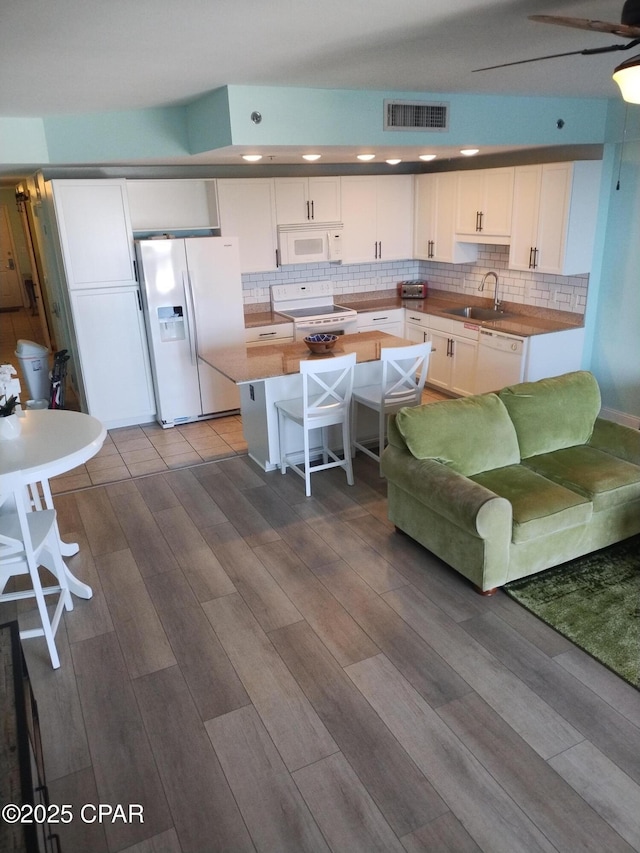 kitchen with white appliances, a sink, visible vents, white cabinets, and backsplash