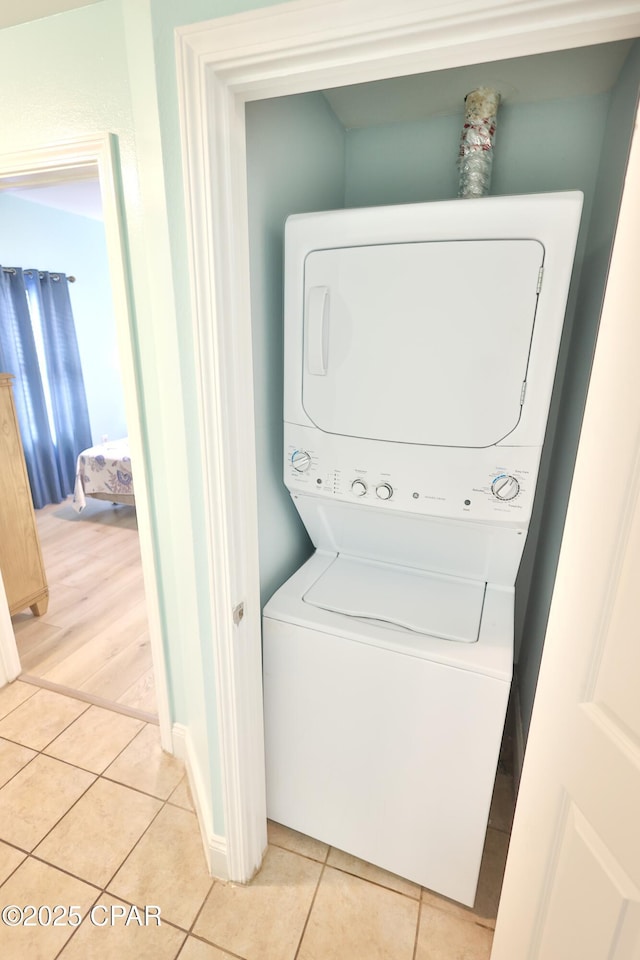 laundry area featuring light tile patterned flooring, laundry area, baseboards, and stacked washer and dryer