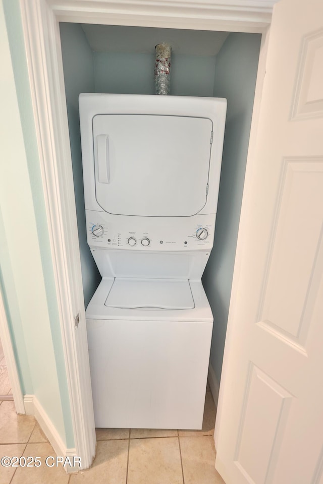 laundry area featuring light tile patterned floors, laundry area, stacked washer / drying machine, and baseboards