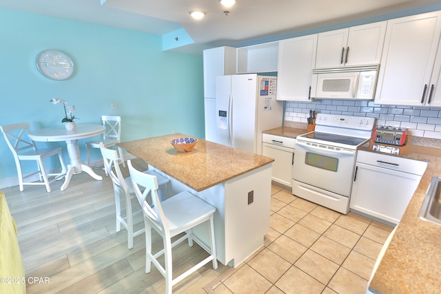 kitchen with a kitchen bar, a kitchen island, white cabinetry, white appliances, and decorative backsplash