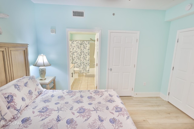 bedroom featuring light wood-type flooring, baseboards, visible vents, and ensuite bath