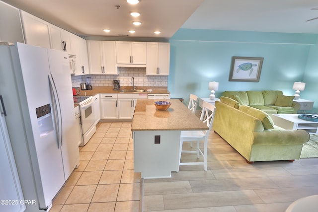 kitchen featuring white appliances, a sink, a kitchen bar, tasteful backsplash, and a center island