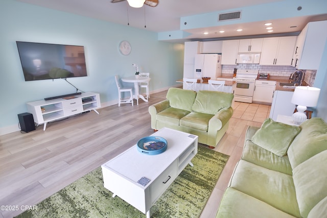living area with light wood-style flooring, a ceiling fan, visible vents, and baseboards