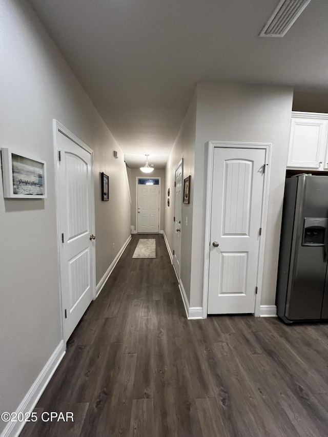 hall with visible vents, dark wood finished floors, and baseboards