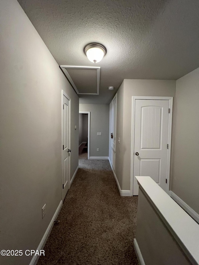 corridor featuring baseboards, dark colored carpet, and a textured ceiling