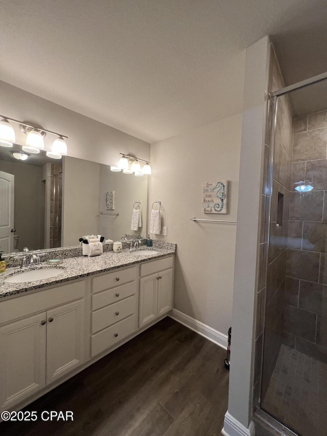 full bath with double vanity, a sink, a shower stall, and wood finished floors