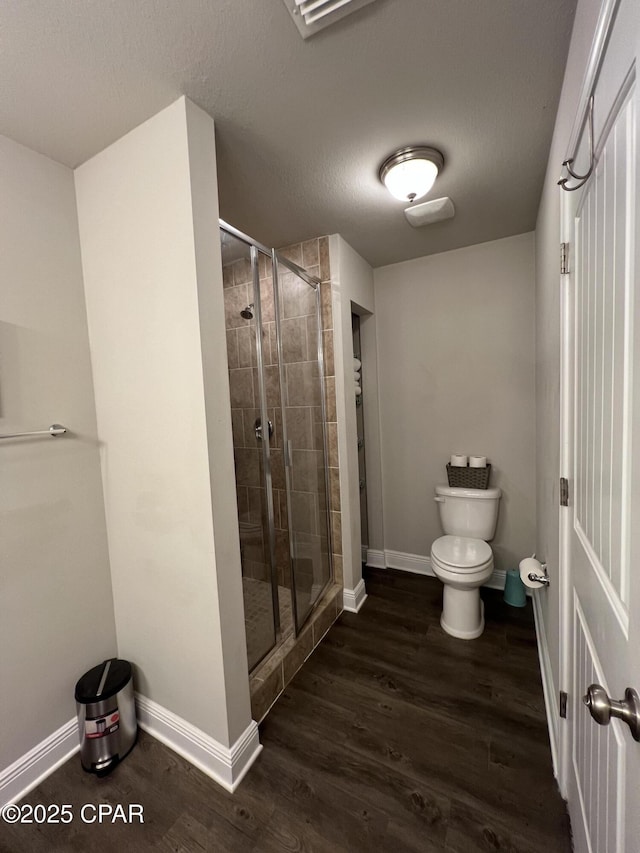 full bath featuring a stall shower, baseboards, toilet, wood finished floors, and a textured ceiling