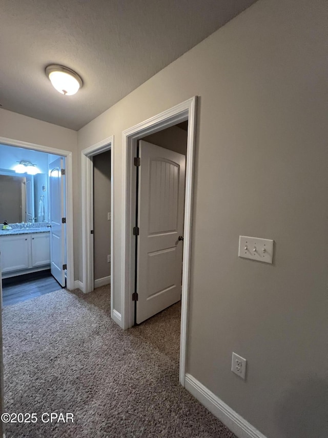 hall featuring carpet floors, baseboards, and a textured ceiling