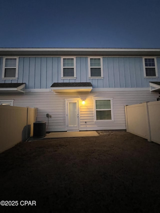 back of house at twilight with board and batten siding, fence, a patio, and central air condition unit