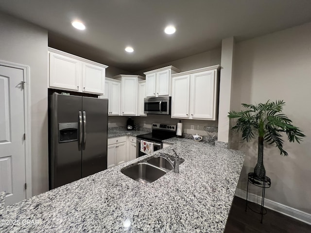 kitchen with appliances with stainless steel finishes, white cabinetry, a sink, a peninsula, and baseboards