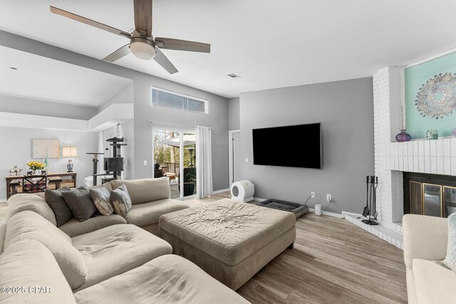 living room with a brick fireplace, baseboards, visible vents, and wood finished floors