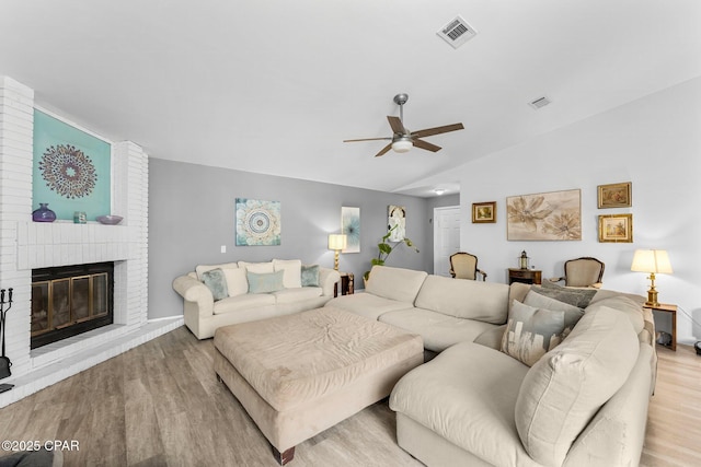 living area featuring a brick fireplace, visible vents, vaulted ceiling, and wood finished floors