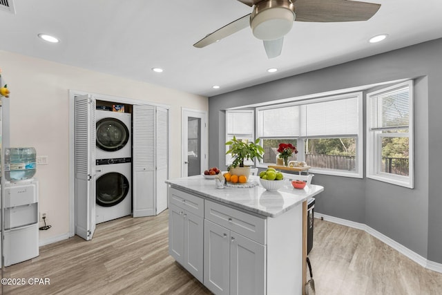 kitchen featuring light stone counters, recessed lighting, baseboards, stacked washer / drying machine, and light wood-type flooring