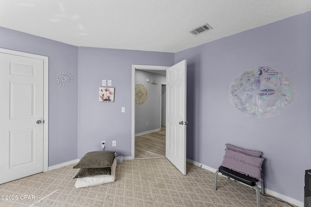 sitting room featuring a textured ceiling, carpet floors, visible vents, and baseboards