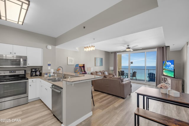 kitchen featuring white cabinets, open floor plan, a peninsula, stainless steel appliances, and a kitchen bar