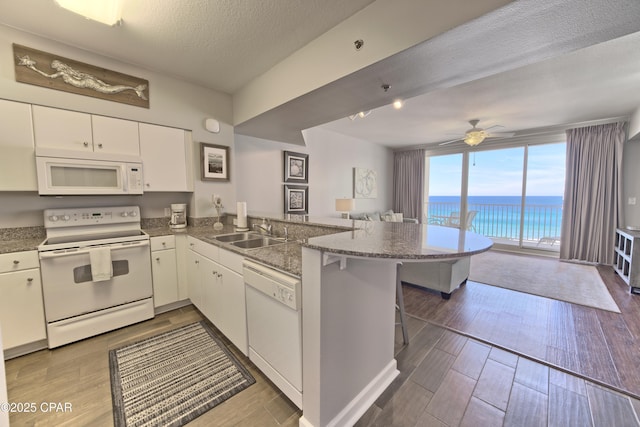 kitchen with white appliances, a sink, a peninsula, and dark wood-style flooring