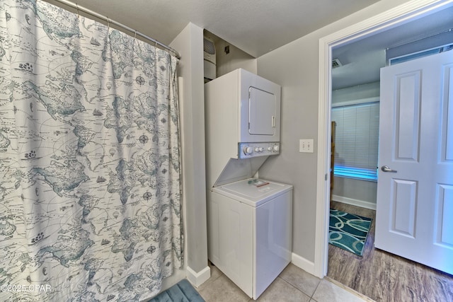 laundry area featuring laundry area, baseboards, stacked washing maching and dryer, and light tile patterned floors