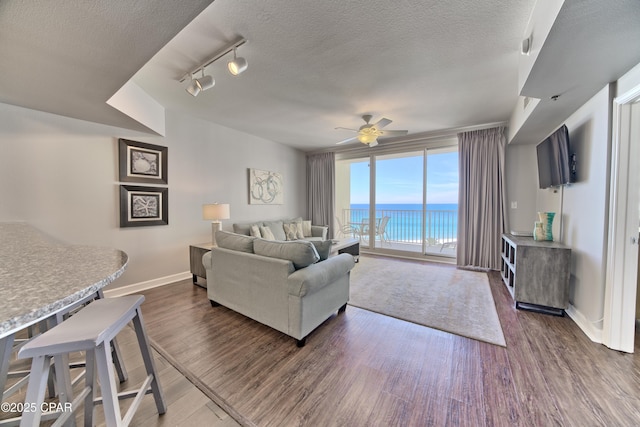 living room featuring a ceiling fan, a textured ceiling, baseboards, and wood finished floors