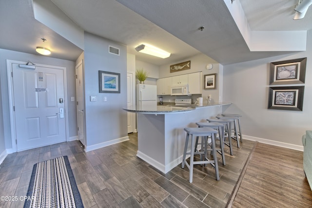 kitchen featuring white appliances, visible vents, white cabinets, a peninsula, and a kitchen bar