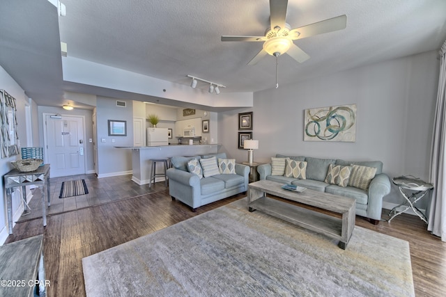 living room featuring dark wood-style flooring, visible vents, a textured ceiling, and baseboards