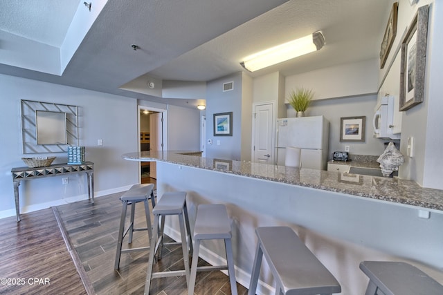 kitchen with white appliances, dark stone counters, a breakfast bar, dark wood-style flooring, and a peninsula