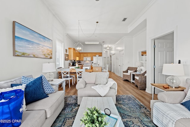 living area with light wood-style floors, a chandelier, visible vents, and crown molding