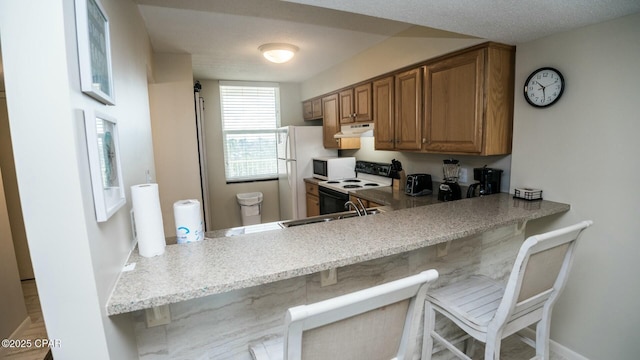 kitchen with brown cabinetry, a sink, white appliances, under cabinet range hood, and a kitchen breakfast bar