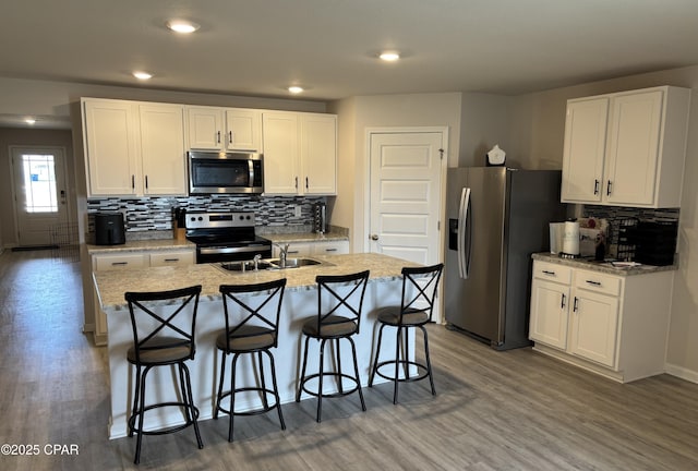 kitchen with appliances with stainless steel finishes, dark wood-style flooring, a center island with sink, and white cabinetry