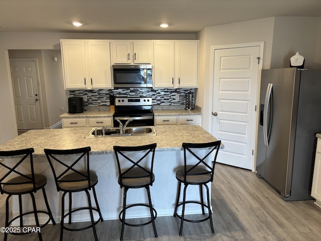 kitchen with light wood finished floors, light countertops, appliances with stainless steel finishes, white cabinets, and a kitchen island with sink