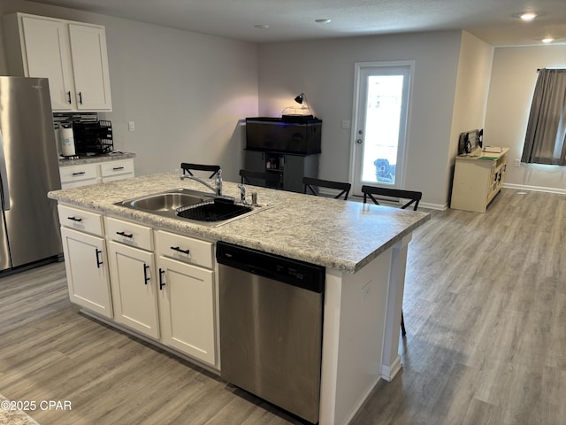 kitchen with light countertops, appliances with stainless steel finishes, white cabinets, a sink, and an island with sink