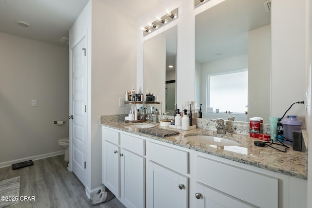 full bathroom with toilet, double vanity, a sink, and wood finished floors