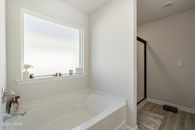 bathroom with baseboards, wood finished floors, a garden tub, and a shower stall