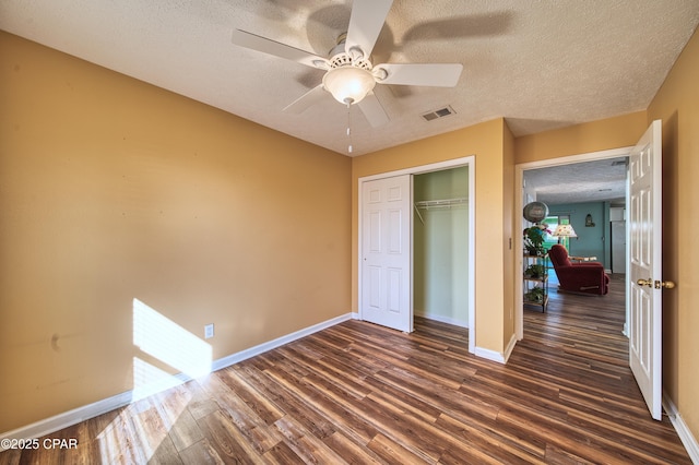 unfurnished bedroom with baseboards, visible vents, dark wood-style flooring, a textured ceiling, and a closet