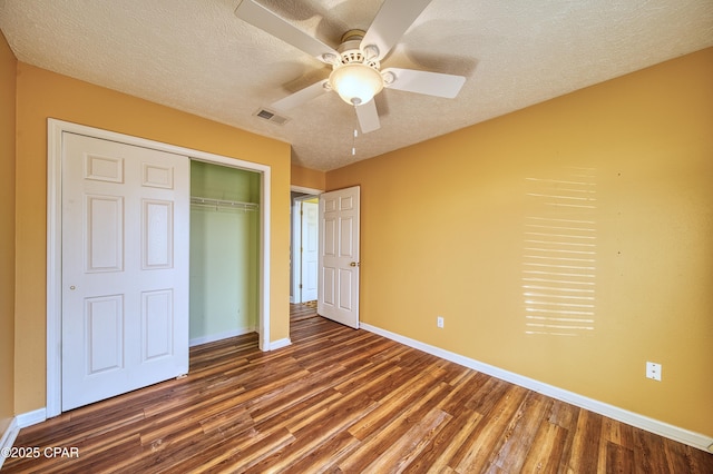 unfurnished bedroom featuring dark wood-style flooring, a closet, visible vents, a textured ceiling, and baseboards