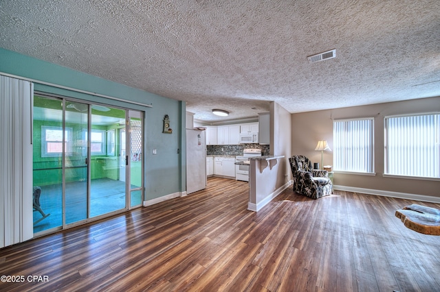 unfurnished living room with a healthy amount of sunlight, visible vents, dark wood finished floors, and baseboards