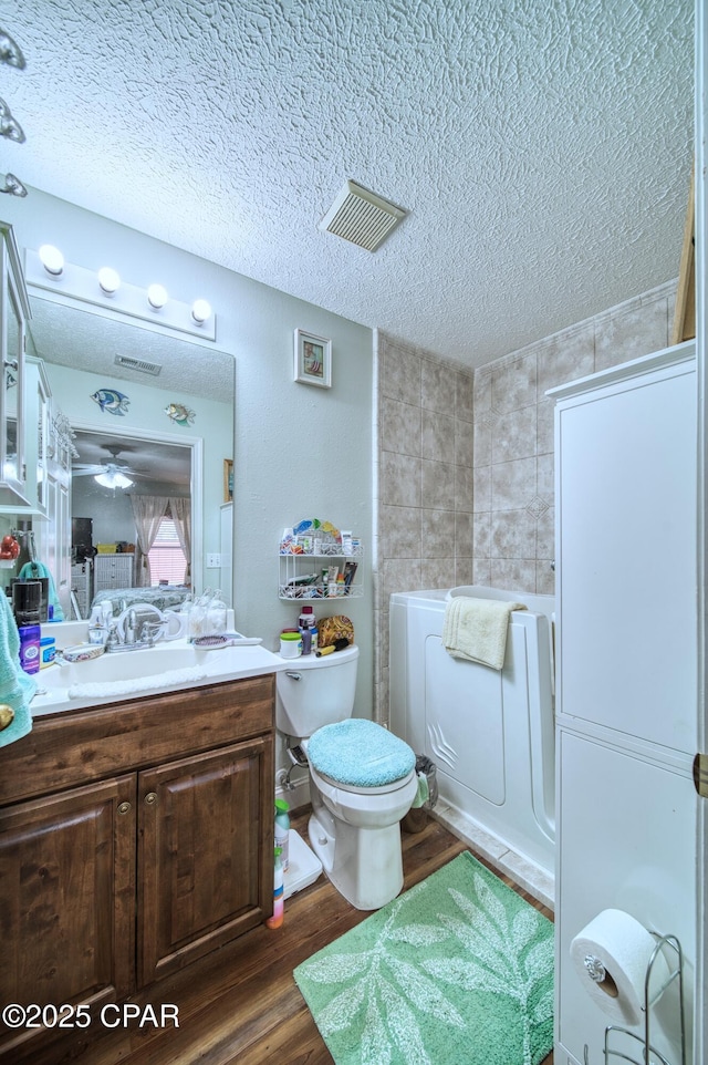 full bathroom featuring a textured ceiling, toilet, wood finished floors, vanity, and visible vents