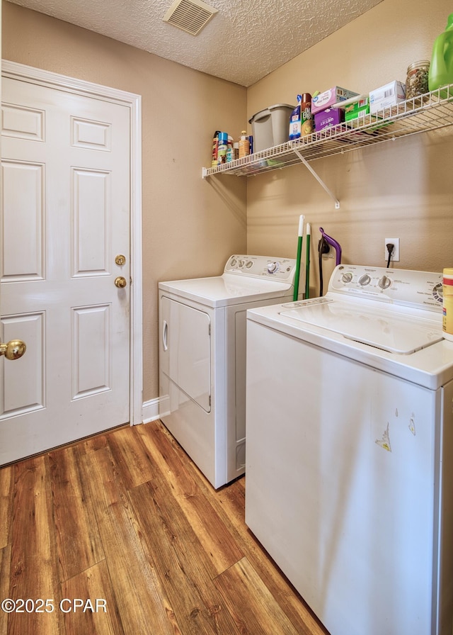 clothes washing area with a textured ceiling, laundry area, visible vents, light wood-type flooring, and independent washer and dryer