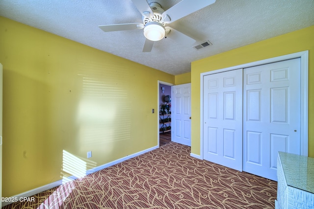 unfurnished bedroom featuring a textured ceiling, dark colored carpet, a closet, and visible vents