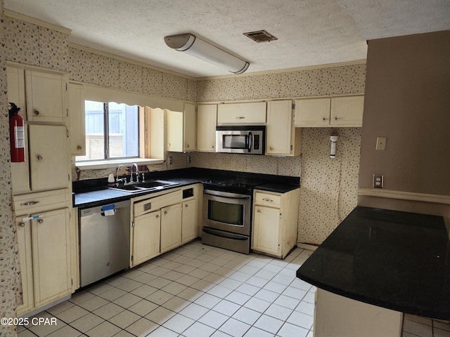 kitchen featuring a textured ceiling, cream cabinets, appliances with stainless steel finishes, dark countertops, and wallpapered walls