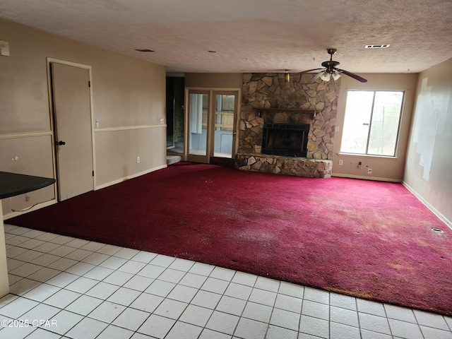 unfurnished living room featuring visible vents, light carpet, ceiling fan, a stone fireplace, and a textured ceiling