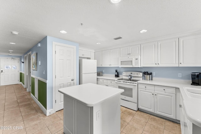 kitchen with white appliances, white cabinets, a kitchen island, light countertops, and light tile patterned flooring