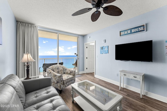 living area with a textured ceiling, dark wood-type flooring, a ceiling fan, baseboards, and floor to ceiling windows