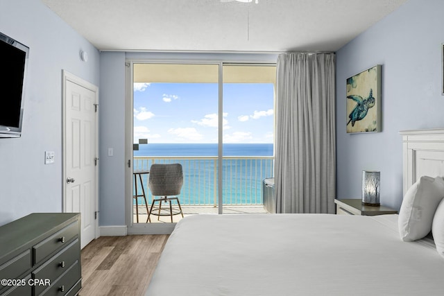 bedroom featuring baseboards, light wood-style flooring, a water view, access to exterior, and expansive windows