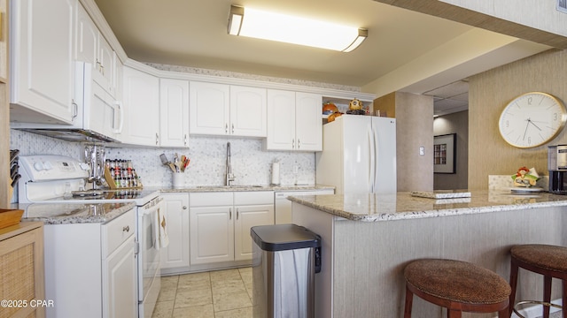 kitchen with a breakfast bar area, white cabinetry, a sink, light stone countertops, and white appliances