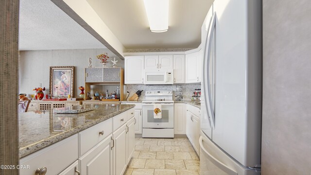 kitchen featuring white appliances, tasteful backsplash, white cabinets, light stone counters, and stone finish flooring