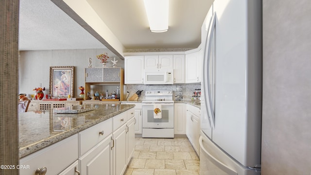 kitchen with stone finish flooring, light stone countertops, white appliances, white cabinets, and decorative backsplash