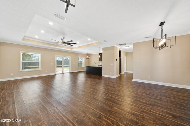 unfurnished living room with crown molding, a tray ceiling, visible vents, and dark wood finished floors