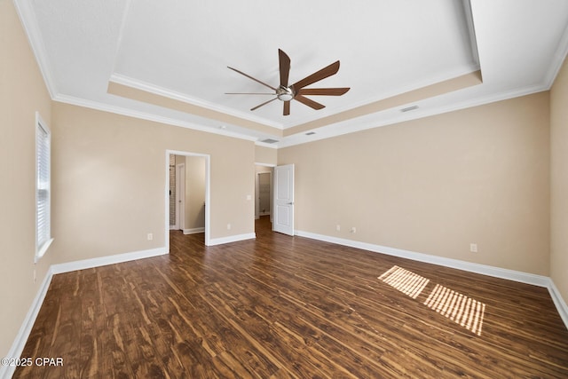 spare room with baseboards, ceiling fan, wood finished floors, a tray ceiling, and crown molding