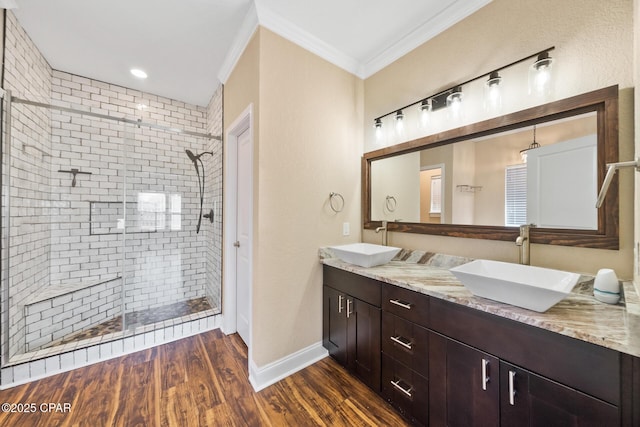 bathroom featuring wood finished floors, ornamental molding, tiled shower, and a sink