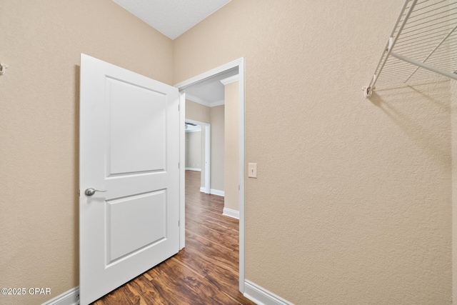 hall with ornamental molding, baseboards, dark wood finished floors, and a textured wall